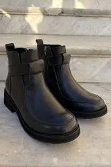 Bota corta de cuero negro con diseño de caña media, cierre lateral y detalle de tira horizontal sobre el empeine. Posee suela de goma gruesa y puntera redondeada.