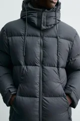 Cazadora acolchada tipo puffer de corte regular, confeccionada en tejido técnico repelente al agua. Cuenta con cuello subido, capucha ajustable y desmontable, cierre frontal con cremallera, bolsillos laterales con cremallera oculta y puños ajustables con tira adherente.