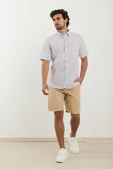 Camisa de manga corta a rayas verticales azules y blancas, con cuello abotonado y cierre frontal con botones marrones.