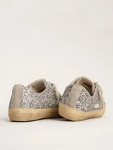 Zapatillas bajas Golden Goose modelo V-Star, cubiertas de glitter plateado, con estrella lateral en cuero color crema y suela de goma color caramelo.
