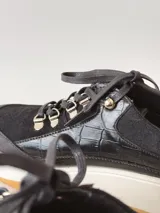 Zapatillas deportivas negras de cuero, con cordones y suela de goma blanca con base marrón.