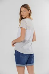 Remera de manga corta con cuello redondo y bolsillo frontal. Presenta un diseño de bloques de color y rayas horizontales: la parte superior (hombros y mangas) tiene rayas finas amarillas, grises y celestes; la parte media es blanca jaspeada con un bolsillo; y la parte inferior es gris jaspeada.