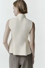 Top de punto sin mangas con cuello subido y diseño peplum con bajo evasé.