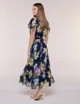 Vestido midi azul marino con estampado floral multicolor, confeccionado en gasa liviana con falda plisada. Tiene escote en V, mangas cortas estilo mariposa y lazo ajustable en la cintura.