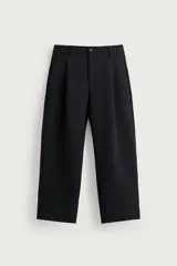 Pantalón relaxed fit marrón oscuro, de corte ancho y recto, con pliegues frontales, bolsillos laterales y cierre con botón y cremallera.
