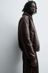 Cazadora oversize de efecto piel color negro, con interior y cuello solapa de pelo sintético gris a contraste. Cuenta con bolsillos de vivo en la cadera, acabados en rib elástico y cierre frontal con cremallera.