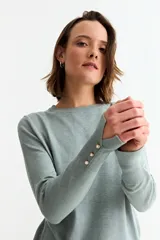 Sweater de punto fino en color verde menta, con cuello redondo, mangas largas y puños acanalados con detalle de botones metálicos laterales.
