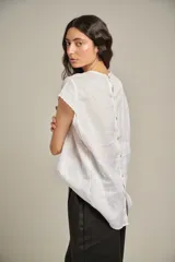 Blusa blanca de lino con cuello redondo, mangas cortas y canesú con alforzas en el frente.