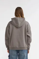 Campera de felpa gris con cierre frontal completo, capucha con cordón ajustable y bolsillos frontales tipo canguro. Presenta diseño holgado, hombros caídos y detalles estampados en rosado en el pecho y la manga.