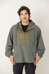 Canguro tipo anorak de color verde militar, con capucha ajustable y cierre frontal parcial. Presenta un panel central en contraste de textura gamuzada y un bolsillo frontal tipo canguro con solapa.