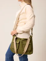 Bolso tipo bandolera de lona color mostaza, con dos bolsillos frontales con solapa y cierre de broche a presión. Cuenta con correas de hombro negras y una correa larga ajustable y extraíble. Presenta herrajes metálicos en tono bronce.