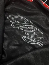 Campera de cuero sintético negro con diseño tipo bomber, cuello camisero y puños y ruedo elásticos. Presenta un bordado grande en la espalda con tipografía cursiva en color blanco.