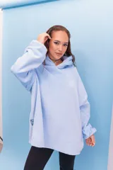 Buzo con capucha de tela de terciopelo en color celeste. Presenta un diseño holgado con aberturas laterales en el ruedo, parche con diseño de sol y texto en la manga, y detalle de logo bordado en el lateral inferior.