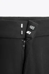 Pantalón negro de tiro medio con pinzas frontales, bolsillos laterales y falsos bolsillos de vivo en la espalda. El bajo termina en puño elástico.