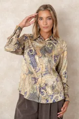 Camisa de satén con estampado paisley en tonos azules, mostaza y beige. Presenta cuello clásico, cierre frontal con botones dorados y puños anchos.