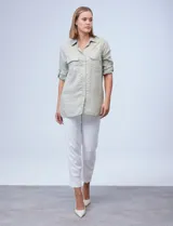 Camisa verde claro con finas líneas verticales blancas, de tencel, con cuello con solapa y abertura central con botones. Tiene dos bolsillos frontales con solapa y botón. Las mangas son largas y regulables con presilla y botón.