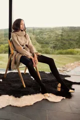 Poncho de tejido de punto grueso en color beige, con cuello alto tipo polera, mangas anchas y terminación con flecos en el ruedo.