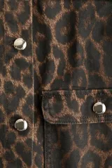 Campera corta de denim con estampado de leopardo en tonos marrón y negro. Diseño sin cuello (tipo 'collar mao') con cierre frontal de botones metálicos plateados y cuatro bolsillos frontales de parche con botón.