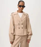 Campera ligera de viscosa color beige, estilo trench corto con doble botonadura, solapas en el cuello, mangas abullonadas con puños elásticos y cintura fruncida con elástico.