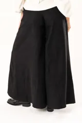 Pantalón de corte palazzo en color negro, con cintura alta, cierre frontal con botón y costuras verticales que definen su estructura amplia.