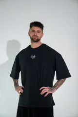 Remera oversize de algodón elastizado en color negro, con diseño gráfico estampado en la espalda que presenta motivos alados y elementos celestiales.