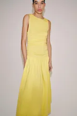 Vestido largo amarillo de algodón, con cuello barco y mangas sisa. Presenta diseño drapeado en los laterales y falda de corte evasé con volumen en el bajo.