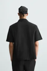 Camisa regular fit de manga corta confeccionada en tejido jacquard con estructura abierta y diseño geométrico. Presenta cuello solapa y cierre frontal con botones al tono.