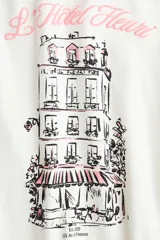 Remera corta entallada de algodón, color blanco, con ribetes rosados en el cuello y mangas, y estampa frontal de un edificio parisino con la inscripción "L'Hôtel Fleuri".