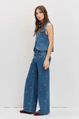 Pantalón de jean azul de tiro medio y corte wide leg, con pequeños bordados de motivos paisley en hilo marrón distribuidos por toda la prenda. Cuenta con bolsillos clásicos, presillas para cinto y cierre frontal con botón y cremallera.
