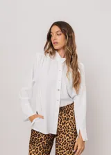 Camisa blanca de cuello redondo con frunces, abotonada y de manga larga con puño abierto.