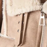 Campera de estilo aviador en color taupe, confeccionada en material símil gamuzado con interior y detalles de bordes en corderito sintético color crema. Presenta cierre frontal, dos bolsillos frontales con solapa y botones metálicos, y cuello solapa.