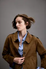 Chaqueta corta de efecto ante en color marrón, con cuello solapa, manga larga y trabillas en los hombros. Presenta cierre frontal con botones y bolsillos delanteros de doble vivo.