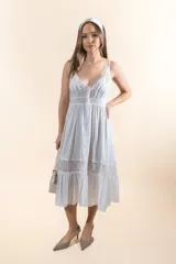 Vestido midi blanco de corte princesa, con breteles finos, escote en V, botones frontales, plisados en el torso y bordados de encaje en cintura y ruedo.
