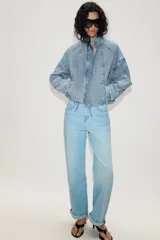 Cazadora bomber de denim con cuello subido, manga larga y cierre frontal con cremallera y botones a presión ocultos. Presenta costuras verticales decorativas y bajo con ajuste elástico.