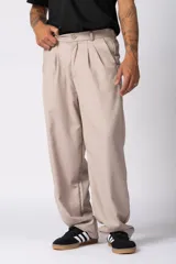 Pantalón sastrero de corte baggy, color beige, con pinzas frontales, cierre de botón y cremallera, y bolsillos laterales.