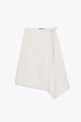 Falda tipo pareo color blanco, de tiro medio, con cierre lateral ajustable mediante lazada y bajo asimétrico.