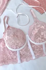 Corset corto de encaje elastizado color rosa pálido, con aros, breteles regulables y detalles de costura blanca en el frente.
