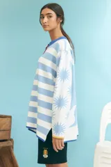 Cardigan de punto con cuello redondo, botones frontales y diseño de rayas horizontales en tonos blanco, celeste, azul, amarillo y rojo. Presenta puños y ruedo en azul.