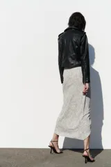 Cazadora biker negra de efecto piel, con cuello solapa, manga larga con trabillas en hombros, bolsillos delanteros con cierre de cremallera, bajo acabado con cinturón a tono con hebilla metálica y cierre frontal cruzado con cremallera.