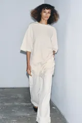 Remera color crema de algodón, corte recto, cuello redondo y mangas cortas. Presenta un panel asimétrico de encaje en el ruedo.