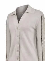 Sweater de punto color beige con cuello camisero y cierre frontal de botones. Presenta mangas largas con detalles de bandas decorativas laterales con perforaciones y terminaciones de crochet en la solapa y cuello.