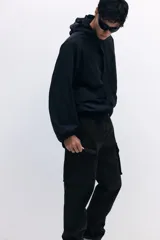 Pantalón cargo negro de nylon, corte recto y holgado, con cintura elástica y cordón ajustable. Presenta bolsillos cargo grandes en las piernas, bolsillos laterales y traseros con cierre, y cordón ajustable en los bajos.