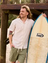 Camisa de manga corta a rayas verticales color beige con finas líneas marrones, cuello tipo cubano y cierre frontal con botones.