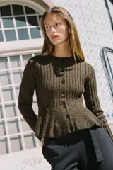 Chaqueta de punto canalé en color verde oliva jaspeado, con cuello redondo, manga larga y cierre frontal con botones. Presenta un diseño entallado con bajo en evasé tipo peplum.