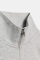 Sudadera crop entallada de color negro, con cuello alto, manga larga y cierre frontal de cremallera metálica. Presenta un diseño corto con bajo asimétrico.