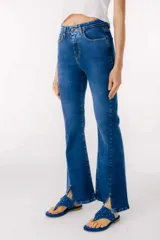 Jean azul claro de corte flare con aberturas en los tobillos y detalles rotos en las rodillas y muslos.