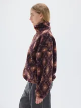 Campera de sherpa con estampado geométrico de rombos en tonos marrones y rosados. Presenta cuello alto, cierre frontal completo en color naranja vibrante y mangas largas con diseño holgado.