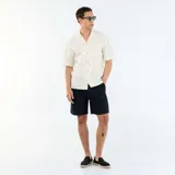 Camisa de manga corta color blanco con sutiles rayas verticales oscuras, cuello camisero tipo cubano y cierre frontal con botones.