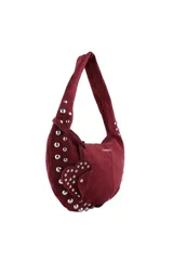 Cartera tipo hobo de gamuza color bordó, con diseño de media luna, decorada con tachas metálicas plateadas en los bordes y un dije colgante en forma de corazón con tachas. Cuenta con cierre superior y logo de la marca grabado en el frente.