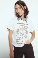Remera blanca de manga corta con estampado gráfico en color marrón que incluye la frase "SLOW MORNINGS CLUB" y dibujos relacionados con el café y el desayuno.